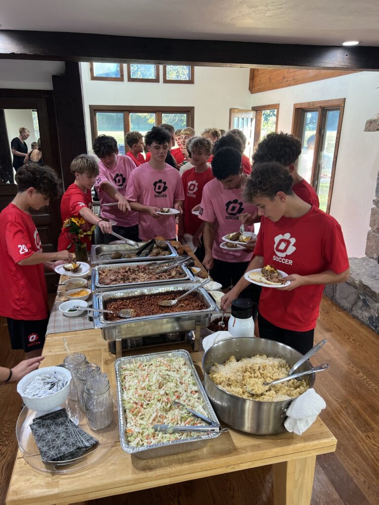 Soccer team at a catered buffet with pulled pork, baked potatoes, beans, coleslaw, and mac and cheese